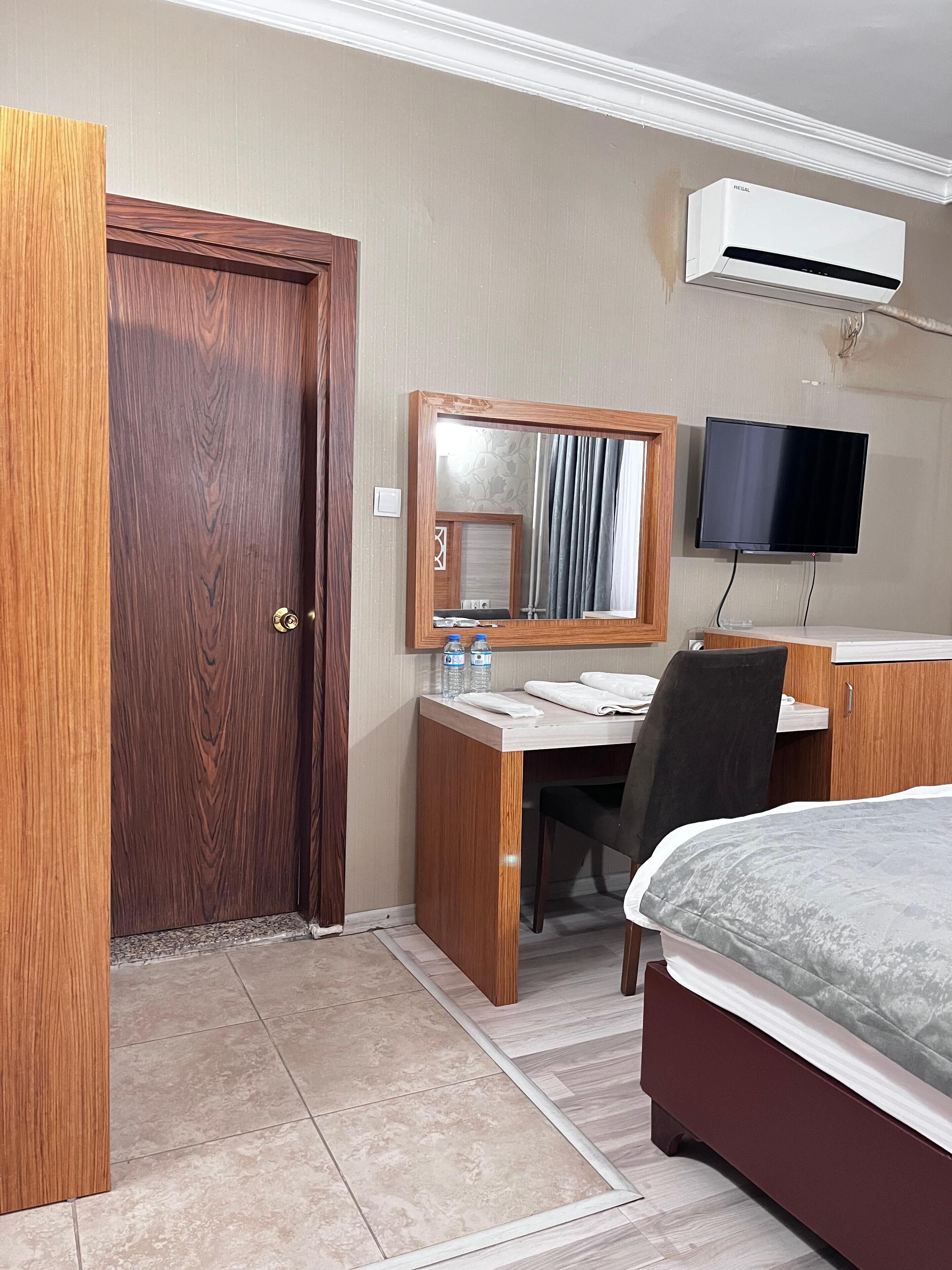 Habitación de hotel con puerta de madera, un escritorio con espejo, televisor de pantalla plana, cama y equipo de aire acondicionado.