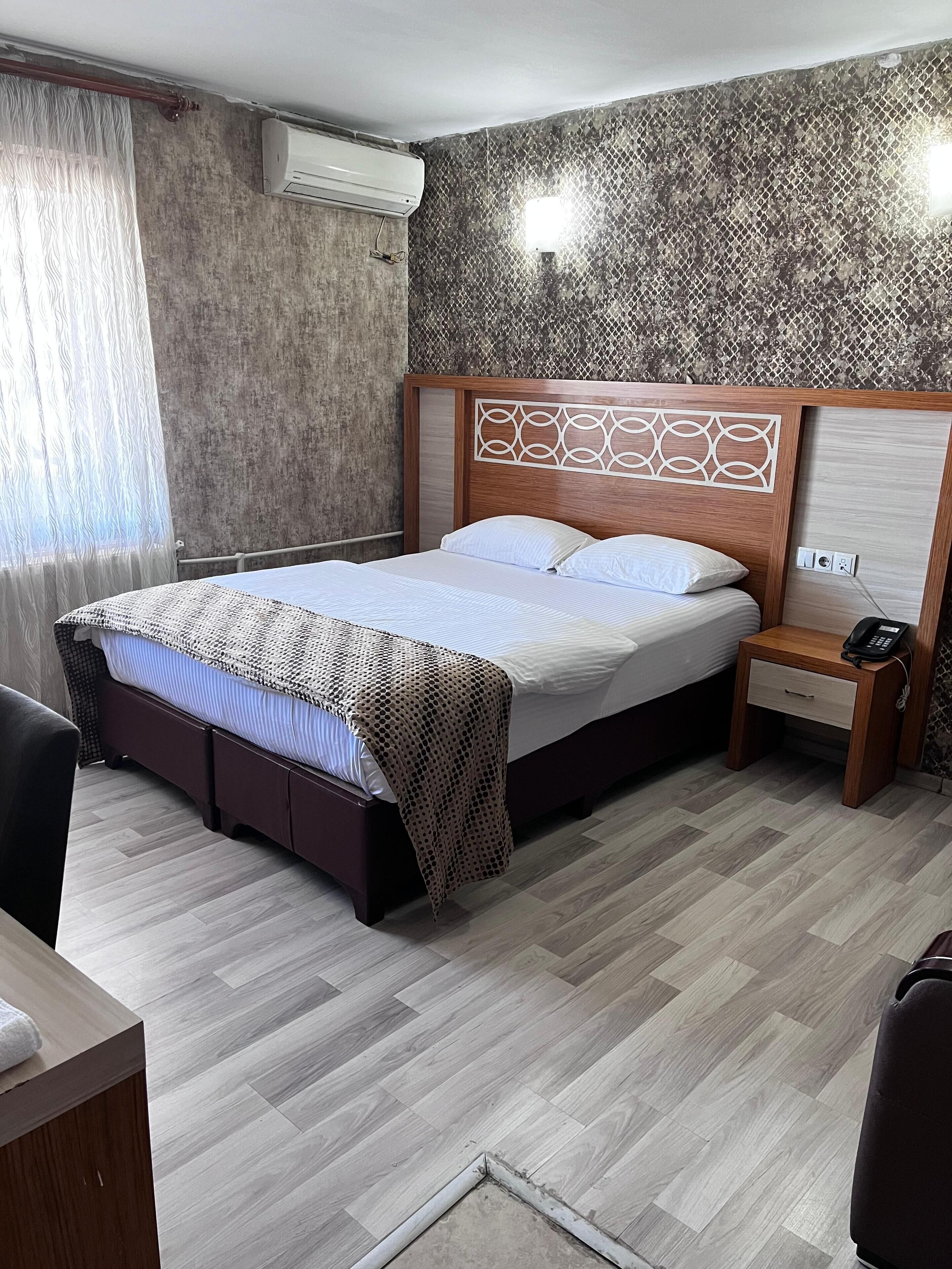 Una habitación de hotel con cama, mesita de noche y aire acondicionado de pared.