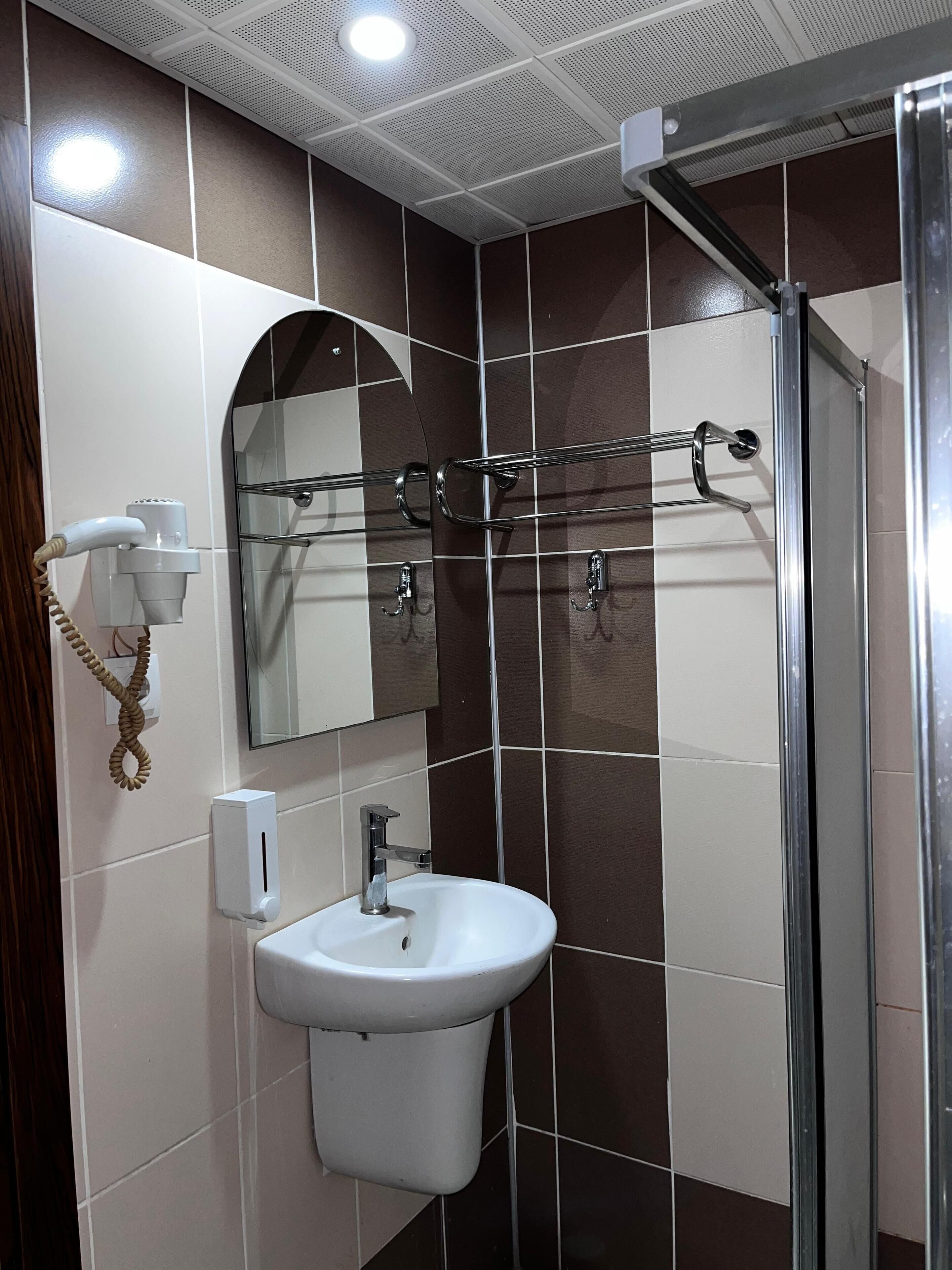 Un bany amb un lavabo blanc, un mirall, un assecador i una dutxa.