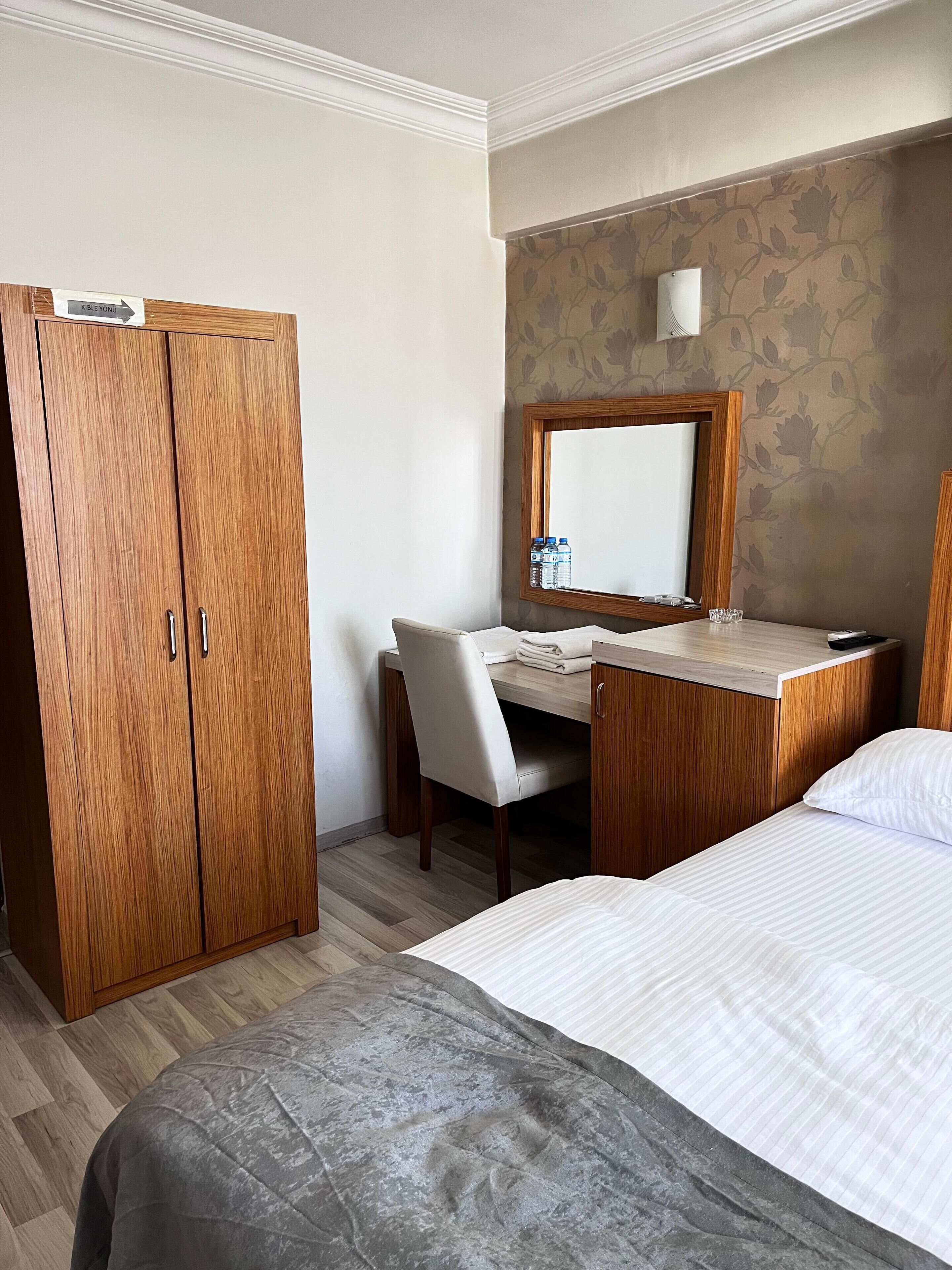 Une chambre d’hôtel avec une armoire en bois, un bureau avec une chaise, un lit et un miroir au mur.