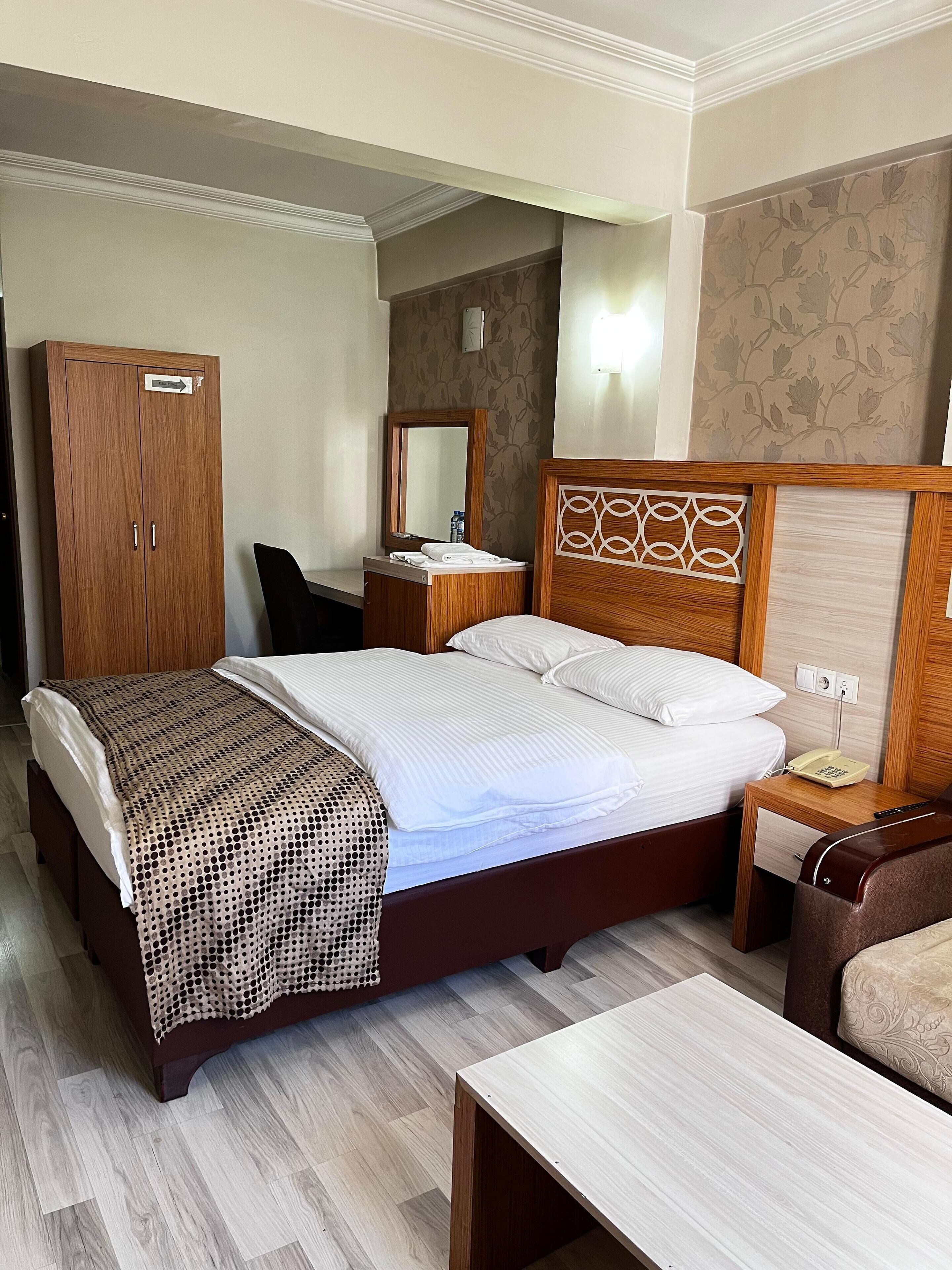 Una habitación de hotel con cama, armario de madera, mesita de noche con teléfono y una silla.