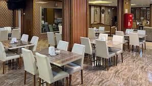A spacious dining area with multiple tables and chairs, a central pillar, and a reception desk in the background.