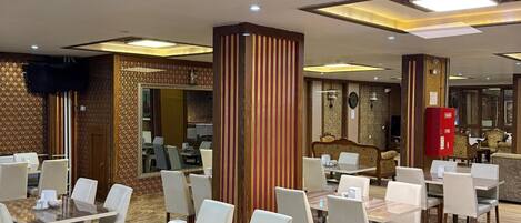 A spacious dining area with multiple tables and chairs, a central pillar, and a reception desk in the background.