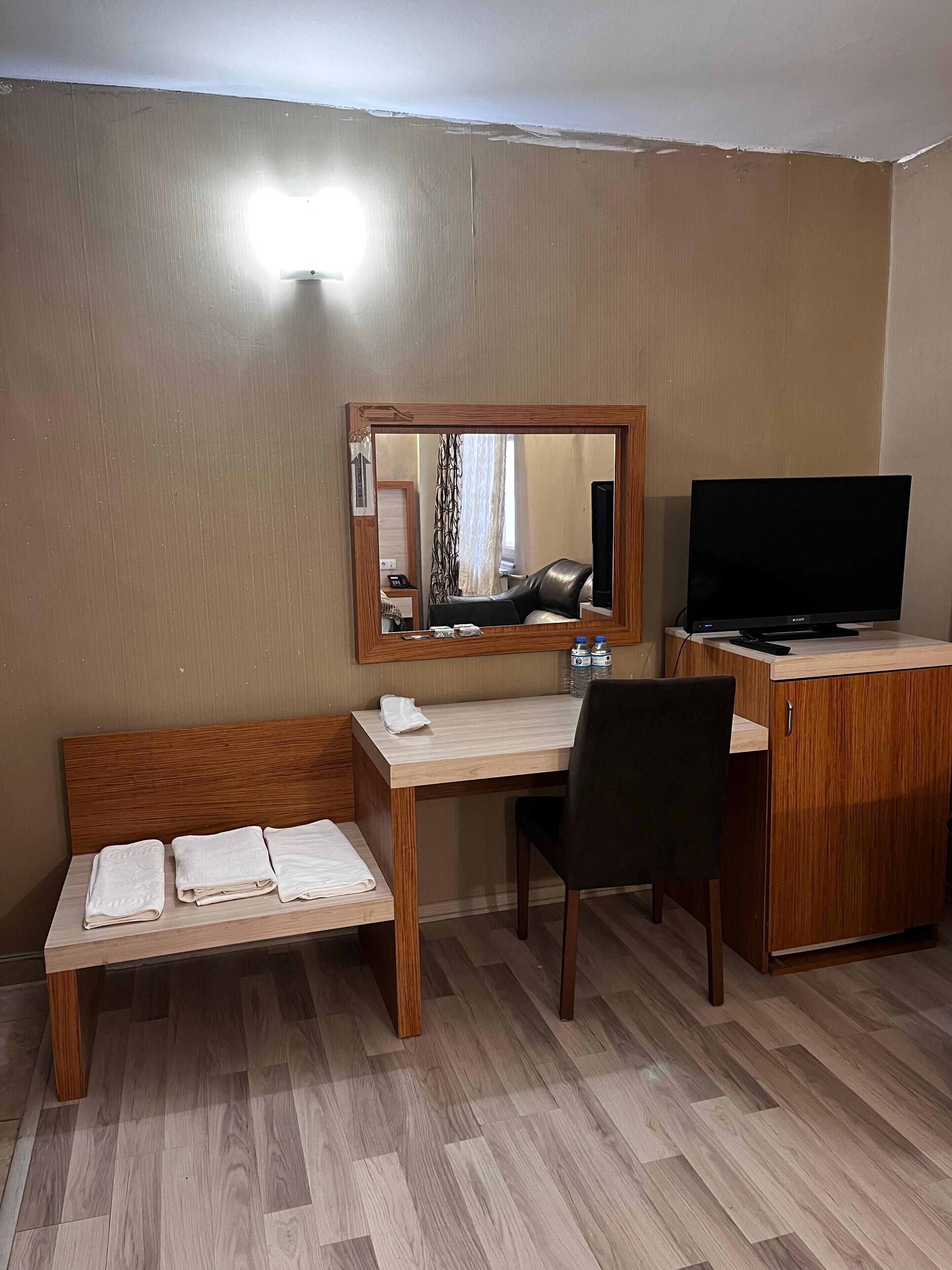 A hotel room with a wooden desk, a chair, a bed with a headboard, a television, and a mirror.