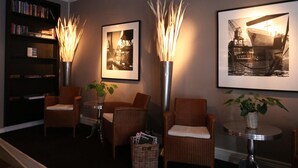 Un hall d’entrée avec des fauteuils en osier, une petite table avec des magazines et des photographies encadrées accrochées au mur.
