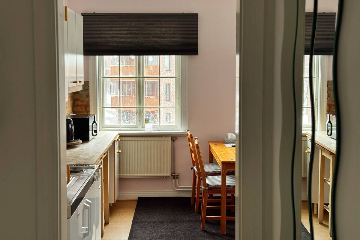 A compact kitchen with a window, a radiator, a table with chairs, and a black rug.