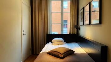 Quarto de hotel com cama, janela com cortinas, porta e um quadro na parede.