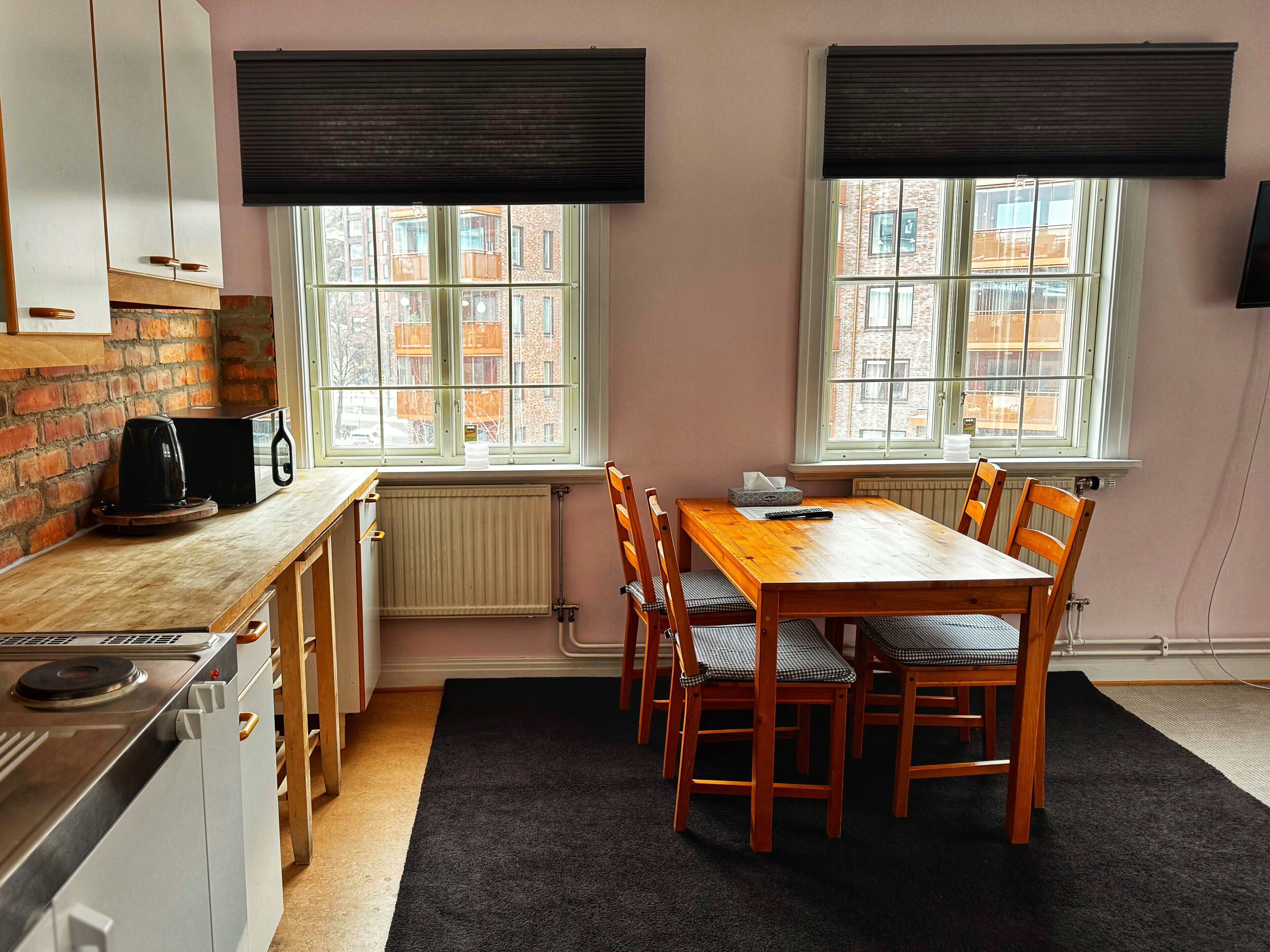 A compact kitchen with a dining area, featuring a wooden table and chairs, a coffee maker, and a stove.