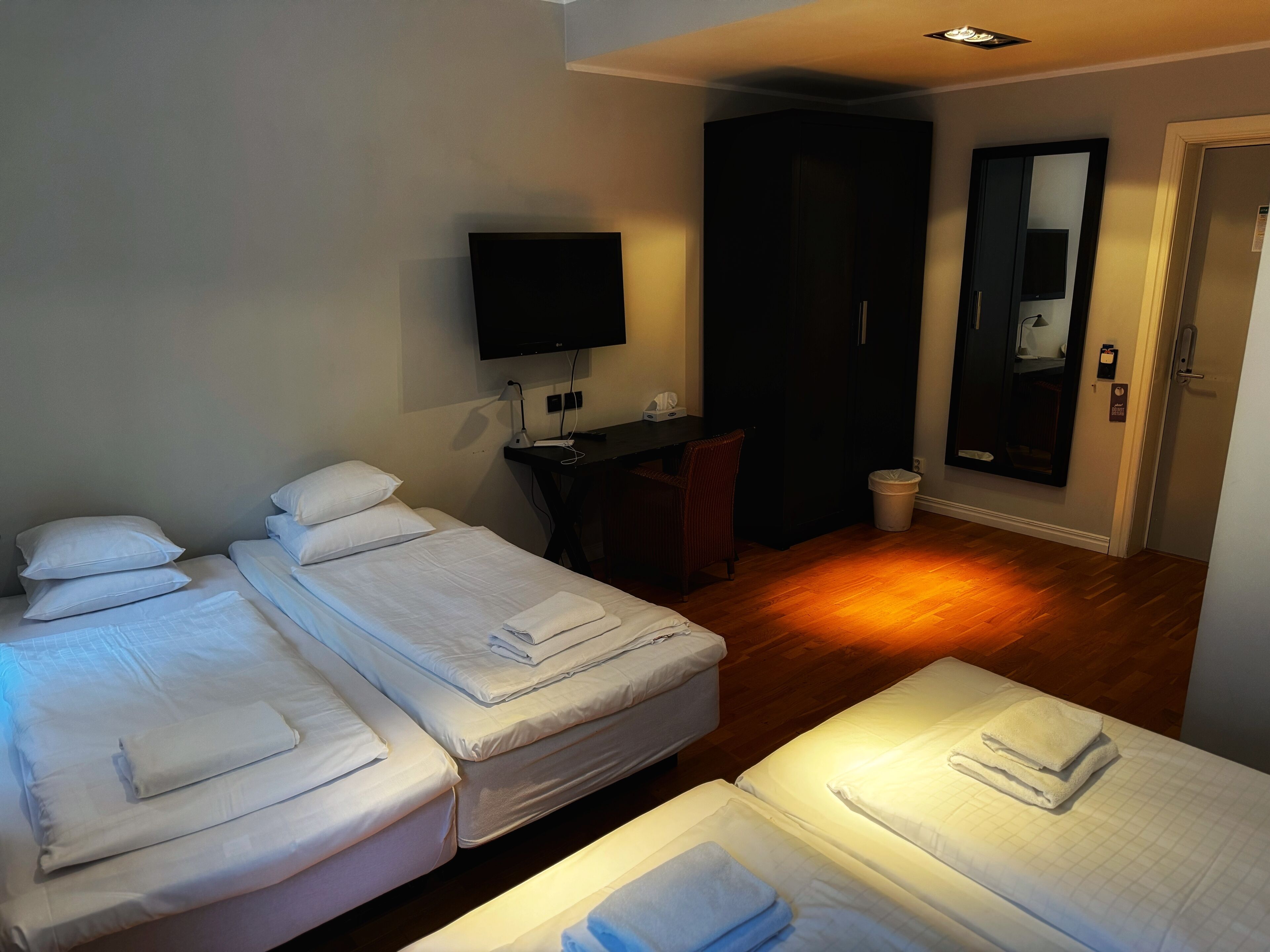 A hotel room with two single beds, a desk with a chair, a television, and a mirror.