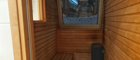 Una sauna de madera con banco, ventana y estufa.