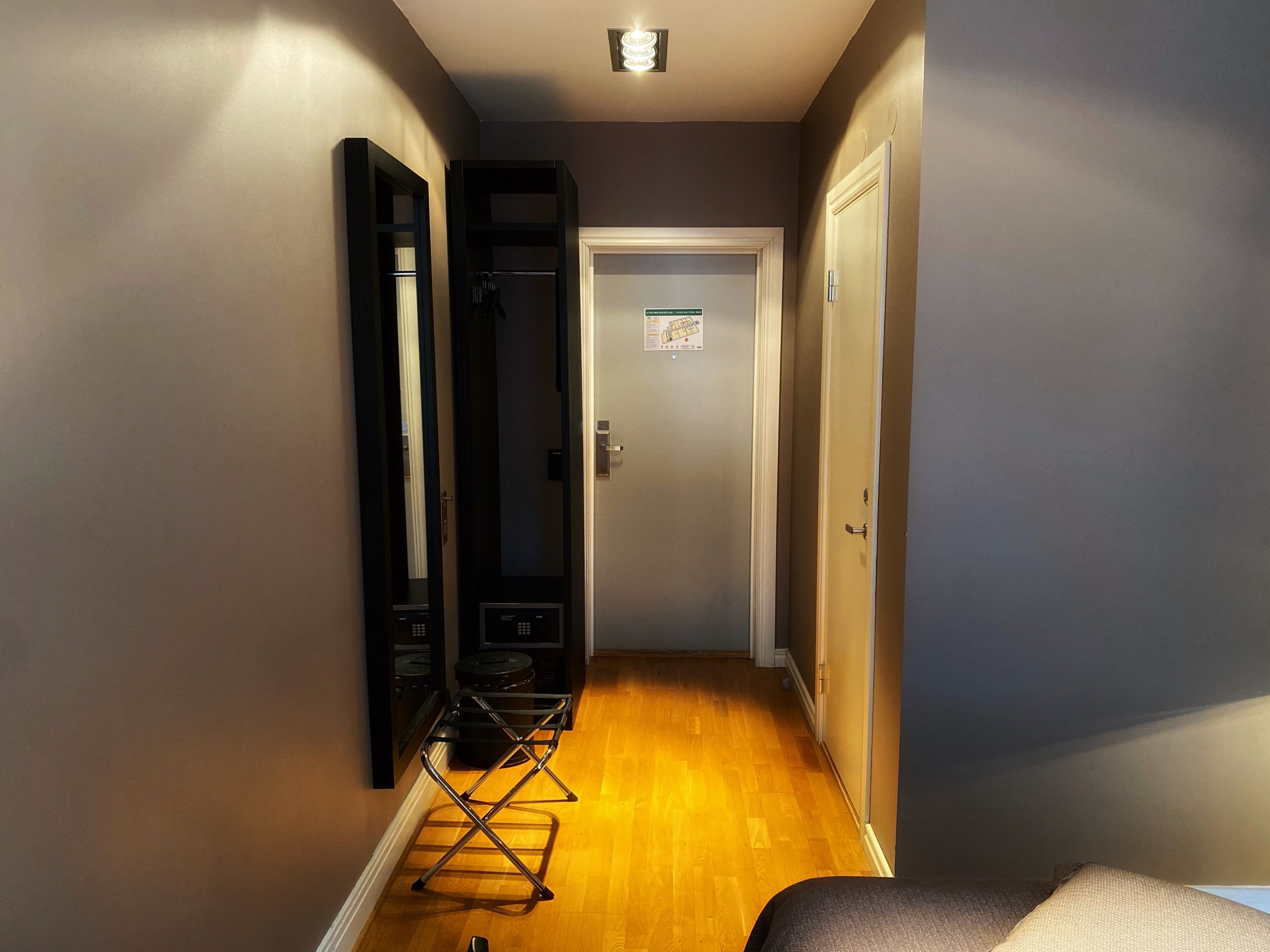 Un couloir étroit au plancher de bois, une porte avec une pancarte et un présentoir métallique.