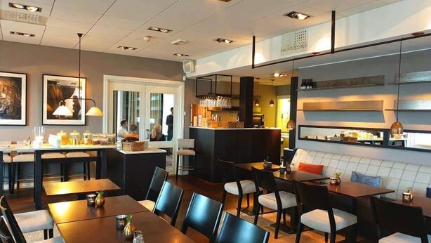 Un espace repas moderne comprenant un bar, des coins salon et une cuisine visible à travers une porte ouverte.