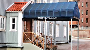 Entrada de hotel com varanda coberta, escadas de madeira e placa indicando "HOTEL VILLAN".