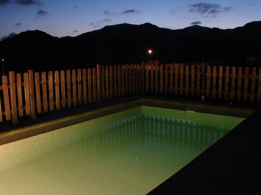Piscina rectangular con borde de azulejos, rodeada de una cerca de madera, con montañas al fondo.