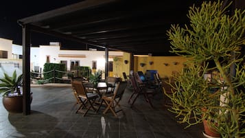 An outdoor patio area with a covered seating arrangement, potted plants, and a view of the surrounding buildings.