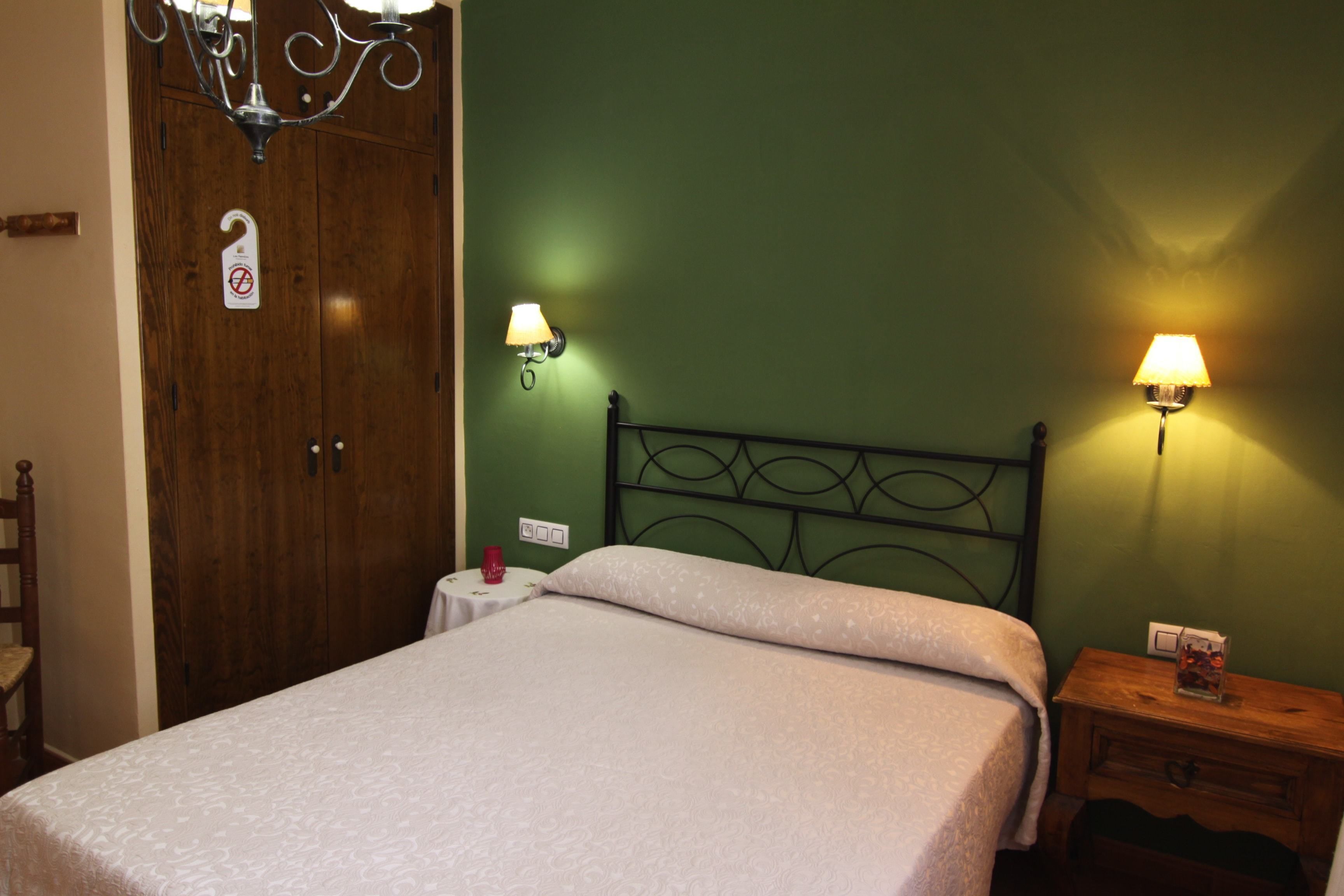 Un dormitorio con cama, armario de madera, dos lámparas de pared, mesita de noche y una silla.