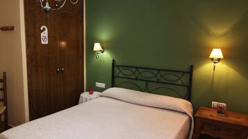 Un dormitorio con cama, armario de madera, dos lámparas de pared, mesita de noche y una silla.