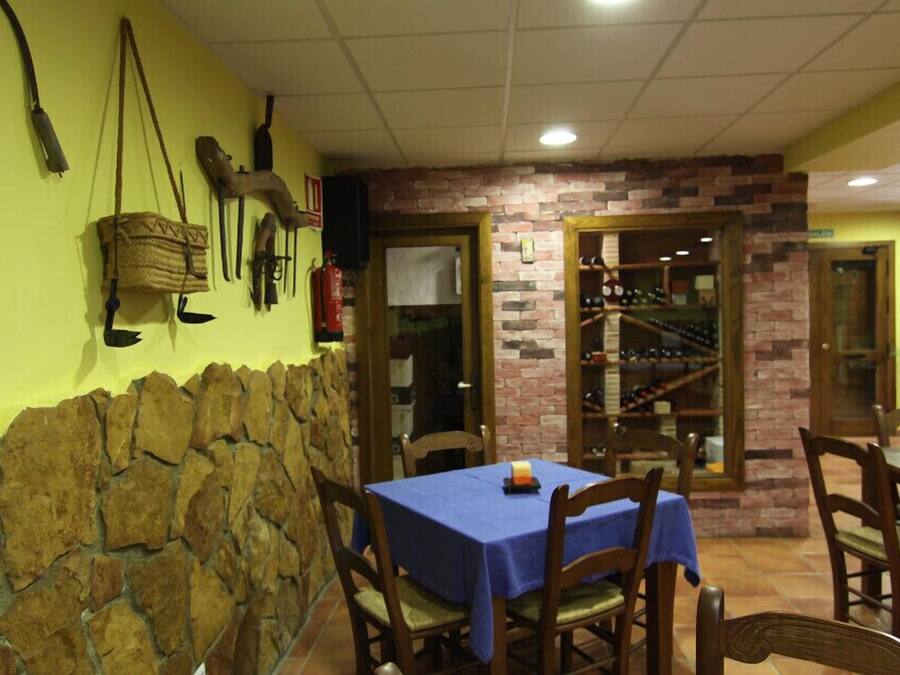 A restaurant with stone walls, wooden chairs, and a blue tablecloth.