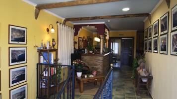 A hallway with a wooden staircase, a reception desk, and framed pictures on the walls.