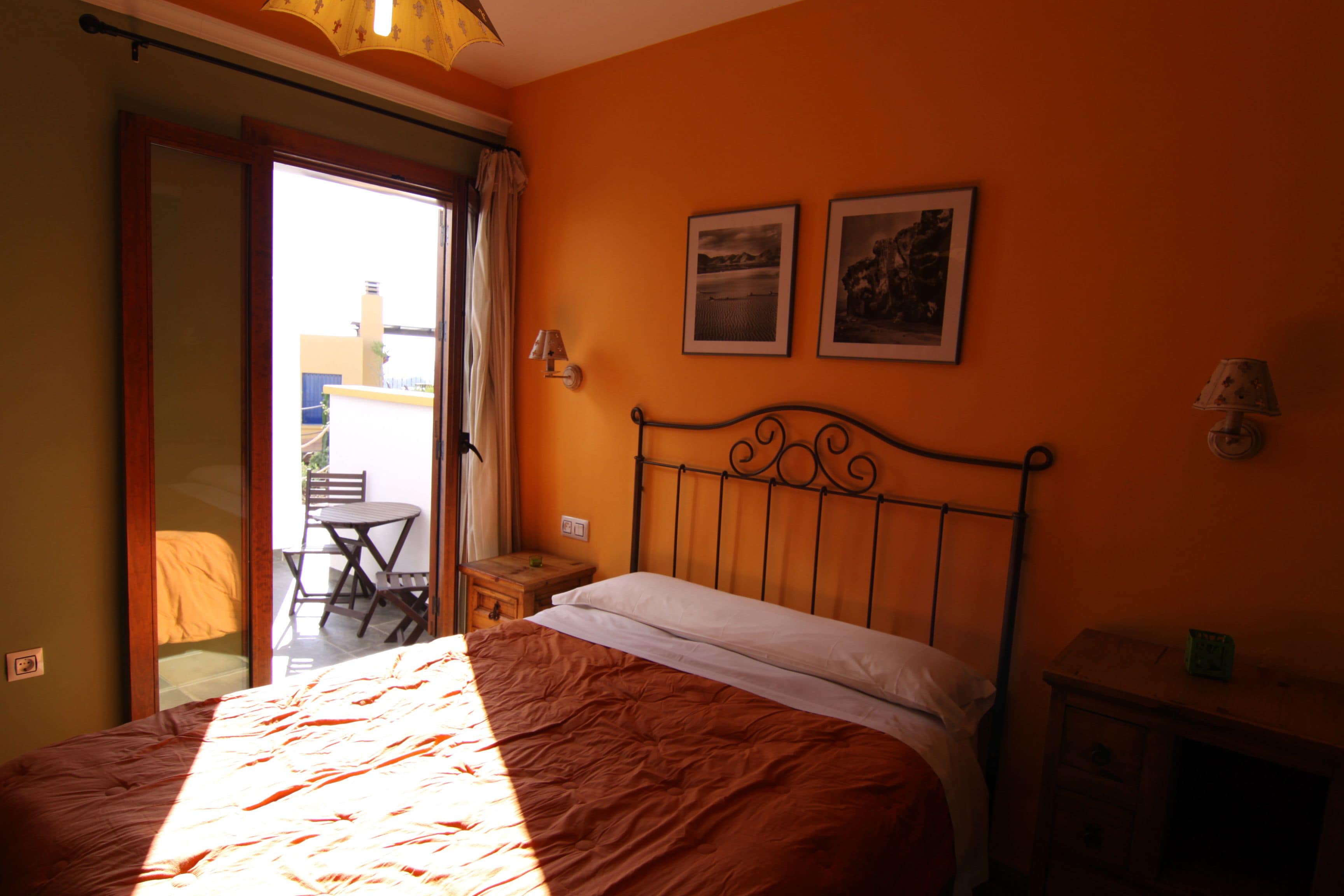 A bedroom with a bed, a nightstand, a lamp, and two framed pictures on the wall.