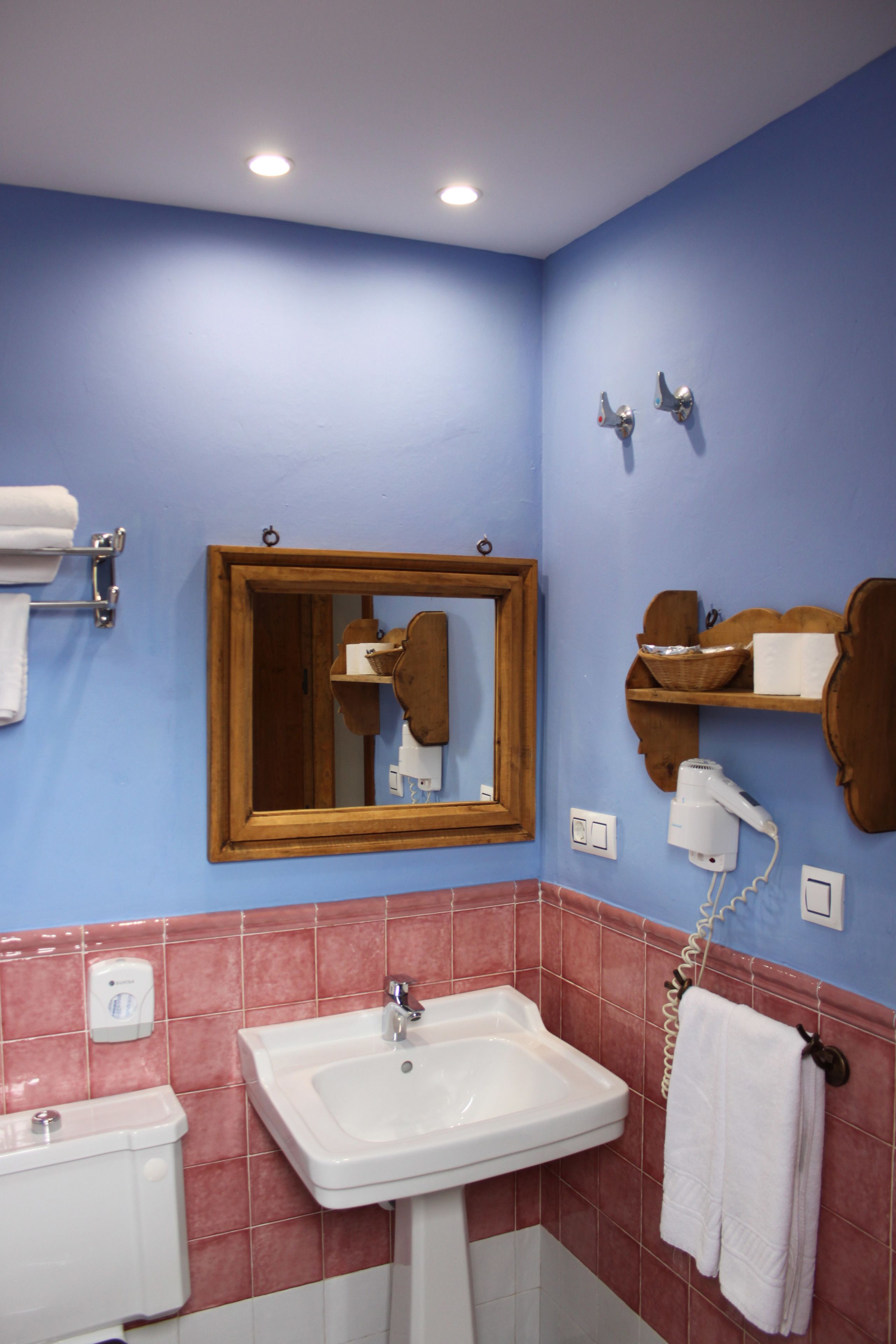 Un baño con lavamanos, espejo, toallero y un secador de pelo en la pared.