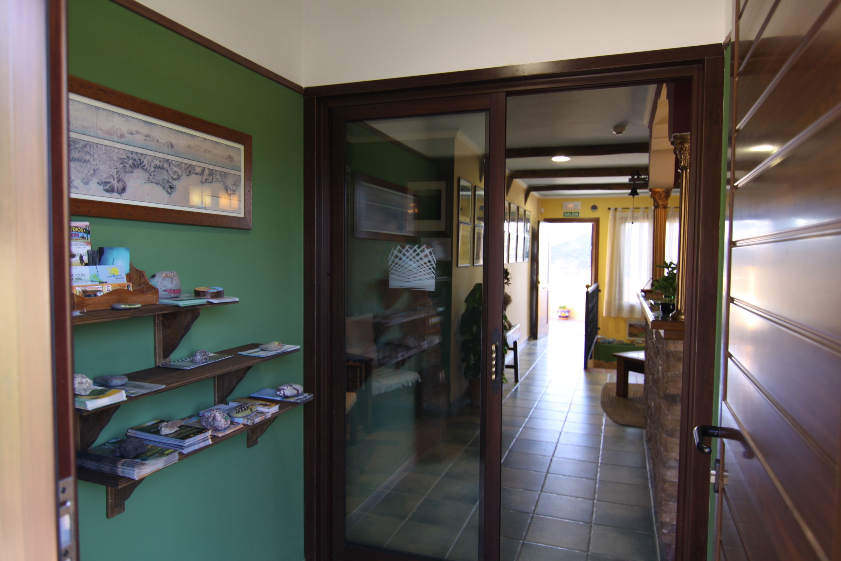 A hallway with shelves displaying books and decorative items, a glass door leading to another room, and a tiled floor.