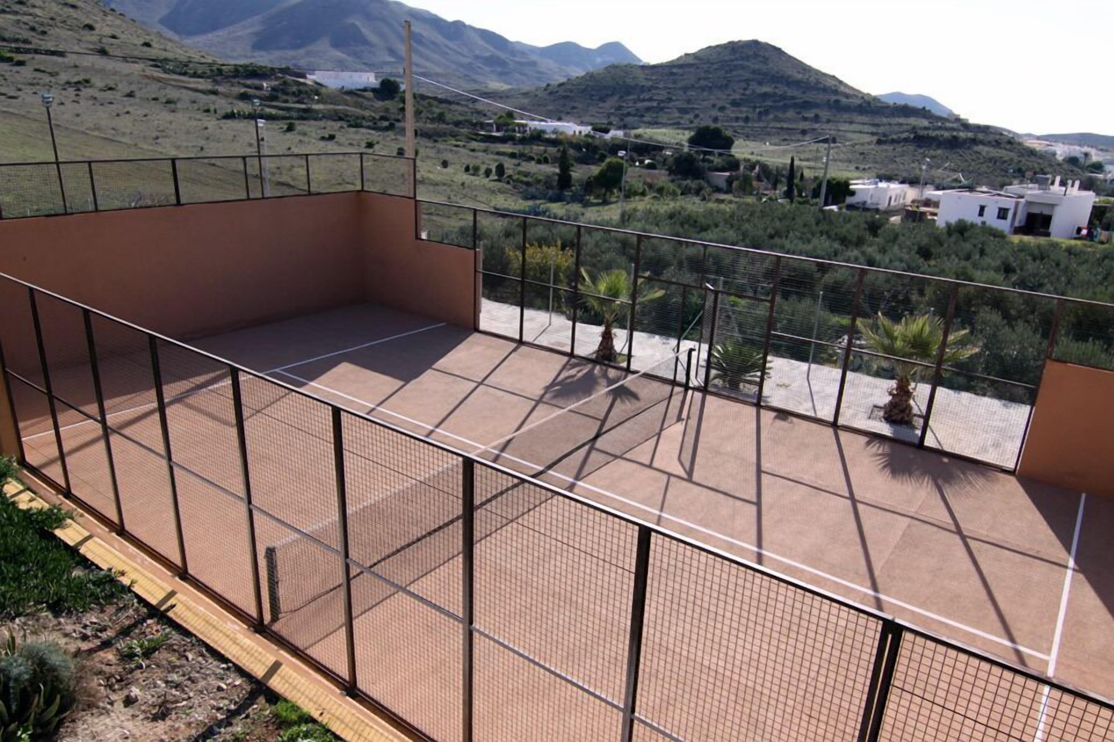 Eine Dachterrasse mit Blick auf eine hügelige Landschaft, einem eingezäunten Bereich und etwas Vegetation.