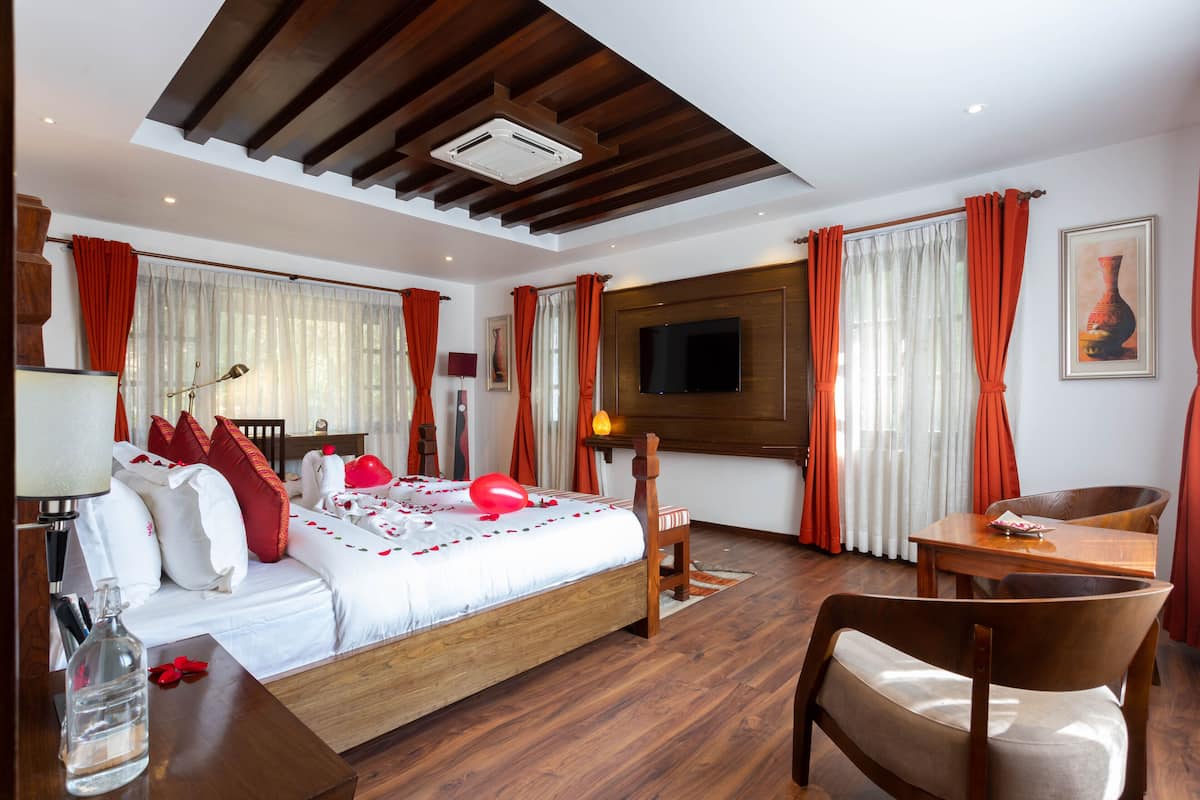 Quarto de hotel com cama, escrivaninha, cadeira, televisão e janela com cortinas.