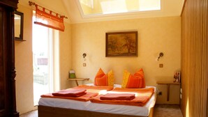 A bedroom with a skylight, a bed with orange bedding, a painting on the wall, and a small bedside table. - Ostsee Ferienhaus Welzin - Altes Schäferhaus (Damshagen)