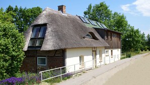 A traditional thatched-roof house with a brick base, large windows, and a small attached wooden structure. - Ostsee Ferienhaus Welzin - Altes Schäferhaus (Damshagen)