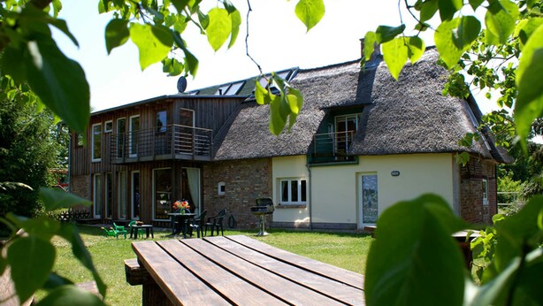 A rustic building with a thatched roof, a wooden deck, and a picnic table. - Ostsee Ferienhaus Welzin - Altes Schäferhaus (Damshagen)