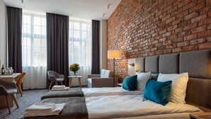 Een hotelkamer met twee bedden, een bureau, een stoel, een lamp en een bakstenen muur.