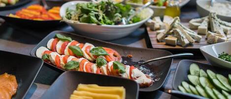 A buffet with various dishes including sliced tomatoes, mozzarella, and cucumbers.
