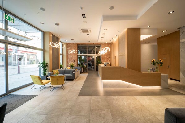 A modern reception area with a wooden reception desk, comfortable seating, and large windows offering a view of the street.