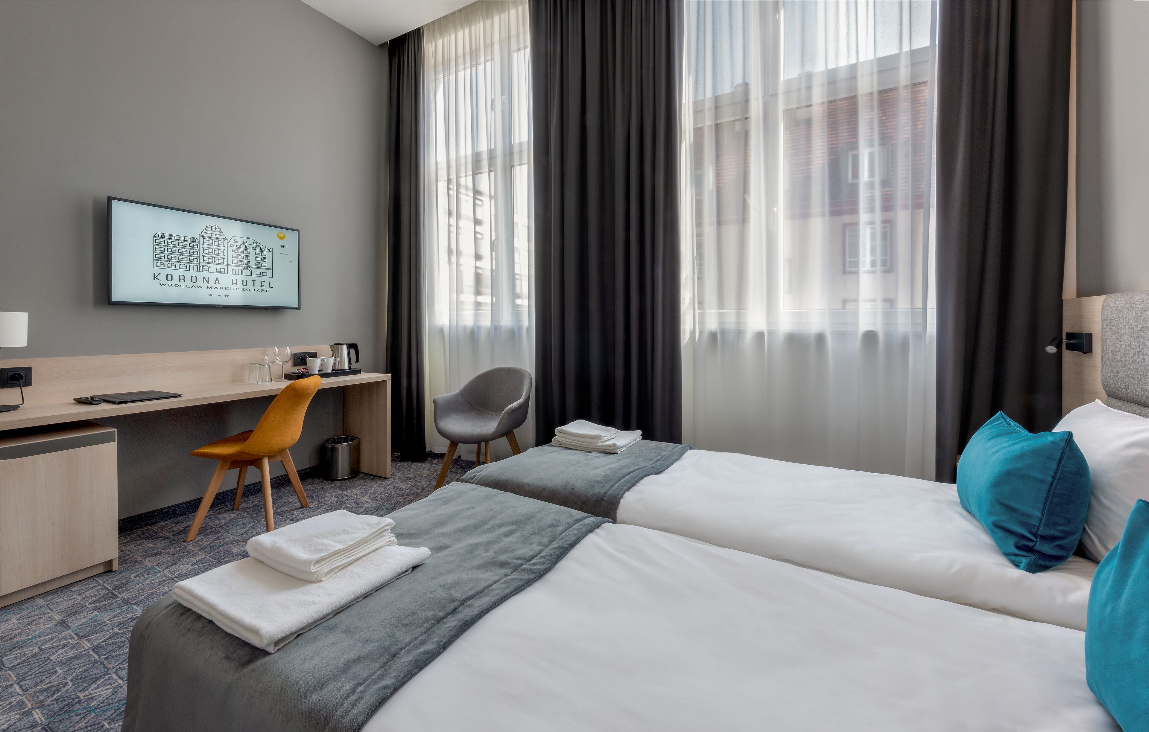 A hotel room with two beds, a desk, a chair, a TV, and a view of the city.