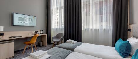 Habitación de hotel con dos camas, un escritorio, una silla, un televisor y vista a la ciudad.