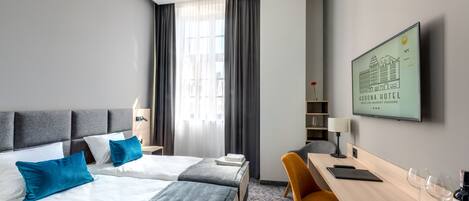 A hotel room with two beds, a desk, a chair, a TV, and a window with curtains.
