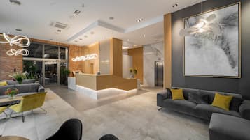A modern hotel lobby with a reception desk, seating area, and a large abstract painting on the wall.