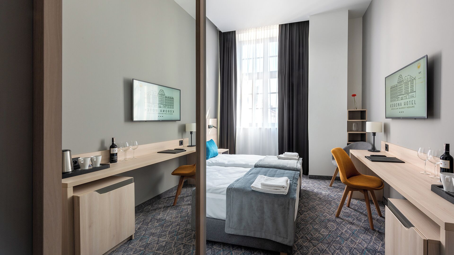 A hotel room with a bed, a desk, a chair, a TV, and a window with curtains.