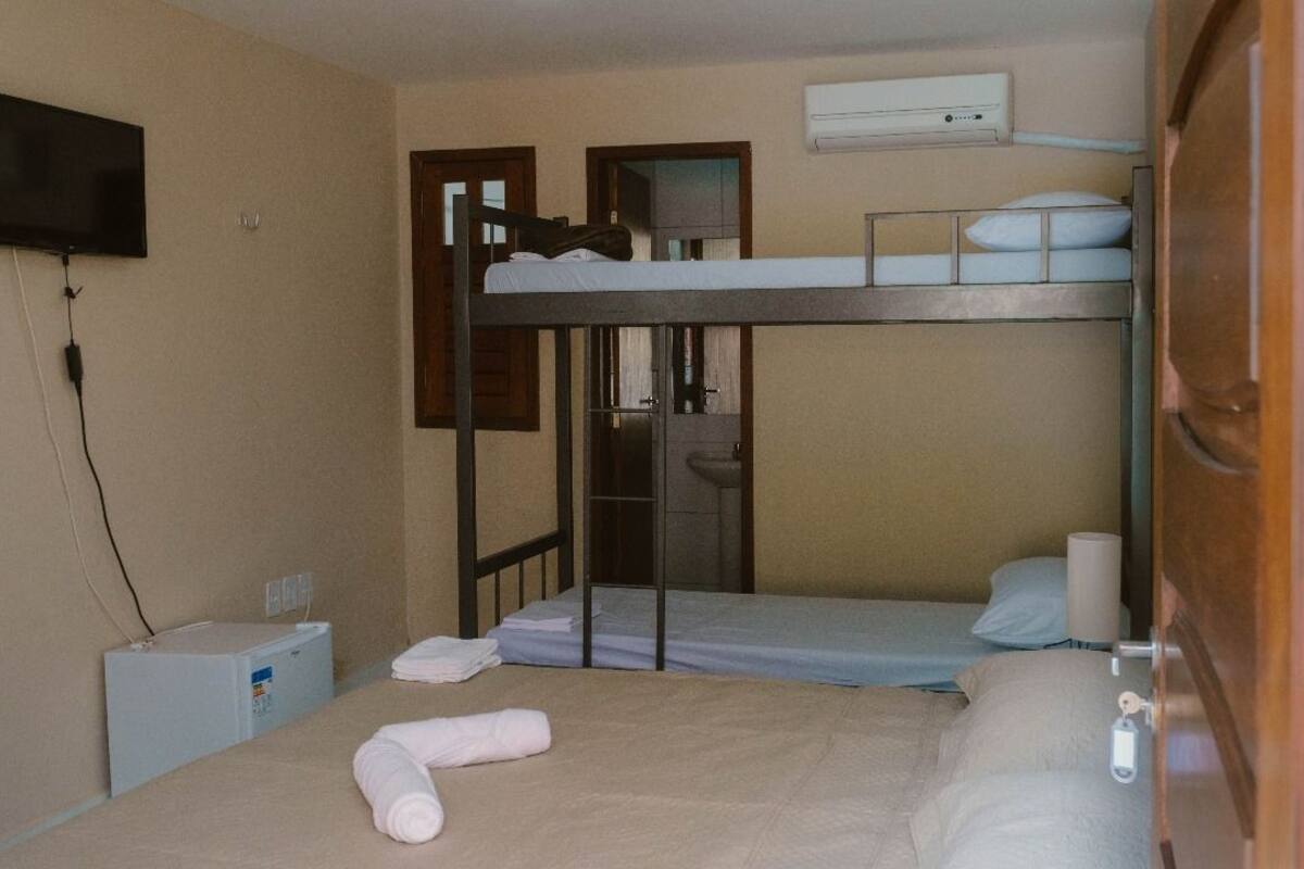Ein Schlafsaalzimmer mit Etagenbetten, einem Fernseher, einer Klimaanlage und einem kleinen Schreibtisch mit Stuhl.