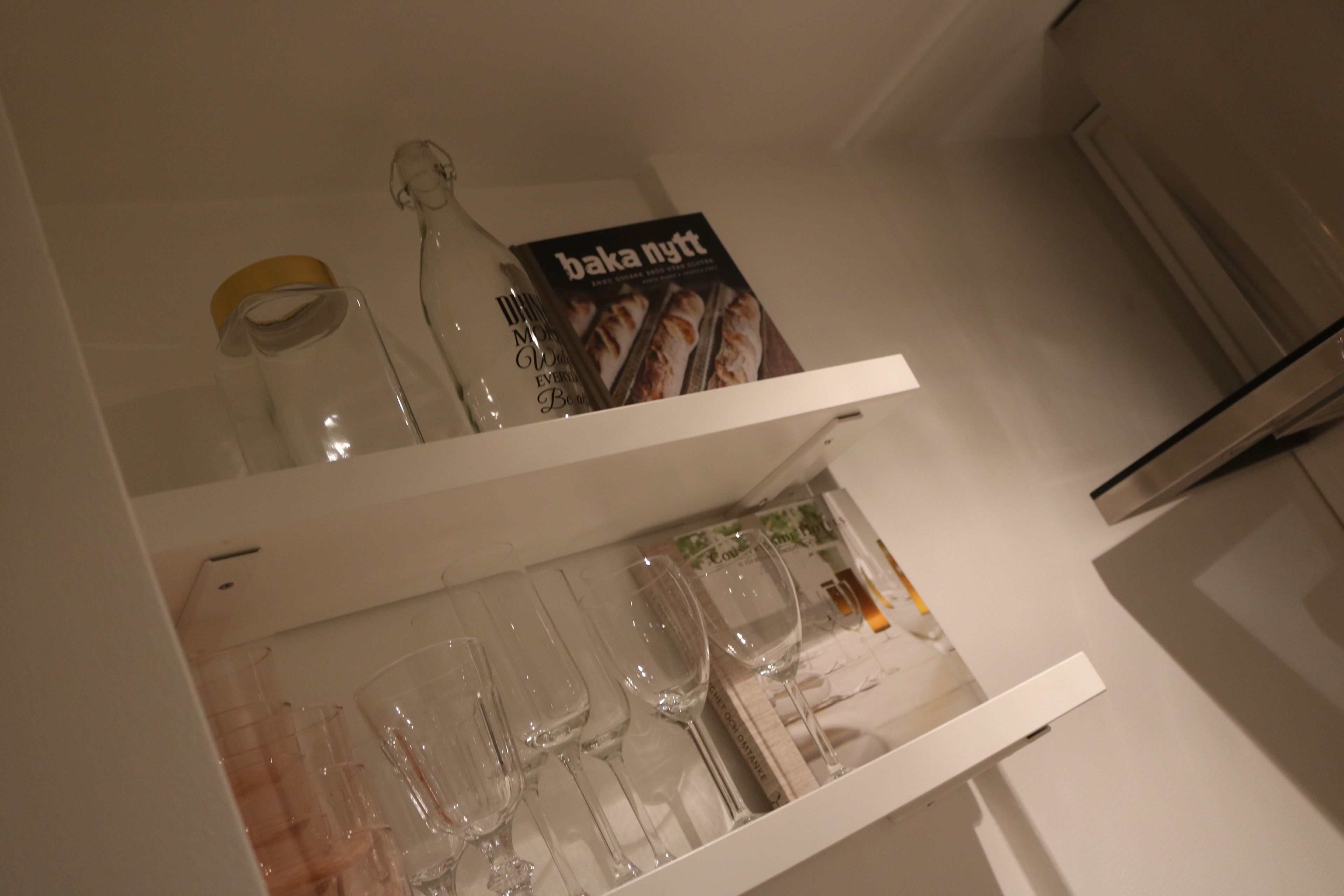 A kitchen shelf with wine glasses, a bottle, and a cookbook.