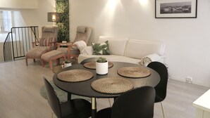 A modern living room with a round dining table, black chairs, a white sofa, and a green wall. - Divine Living - Apartments (Stockholm)