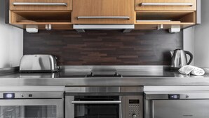 A modern kitchen with stainless steel appliances, wooden cabinets, and a dark wood backsplash. - Divine Living - Apartments (Stockholm)