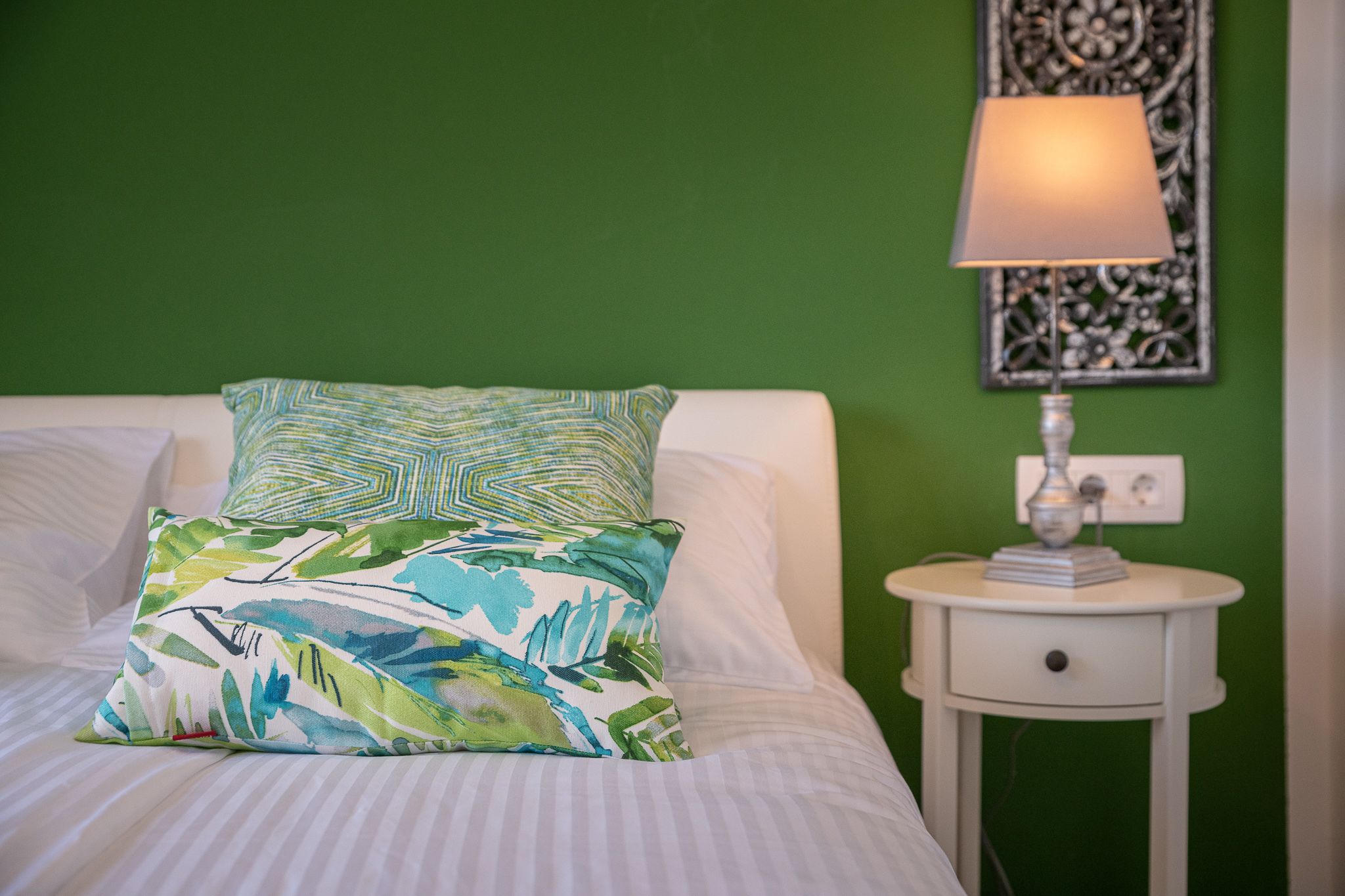 A bed with a patterned pillow, a bedside lamp, and a green wall.