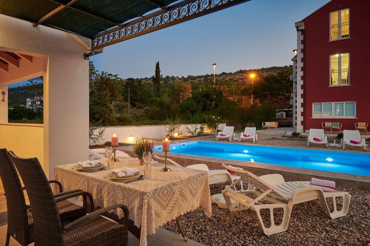 An outdoor pool area with a table set for dining, surrounded by lounge chairs.