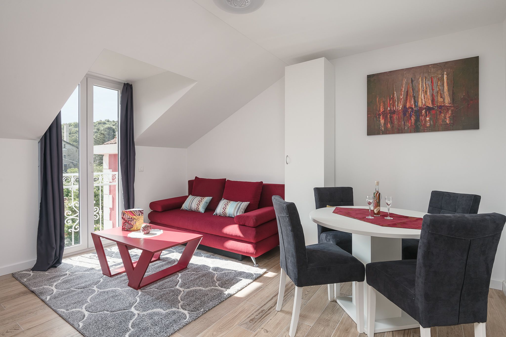 Ein modernes Wohnzimmer mit einem roten Sofa, einem Esstisch mit Stühlen und einem großen Gemälde an der Wand.