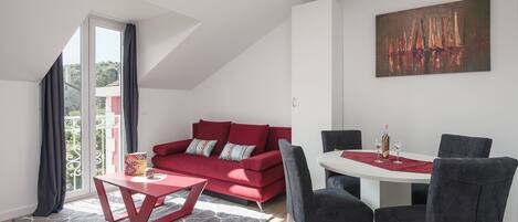 Ein modernes Wohnzimmer mit einem roten Sofa, einem Esstisch mit Stühlen und einem großen Gemälde an der Wand.