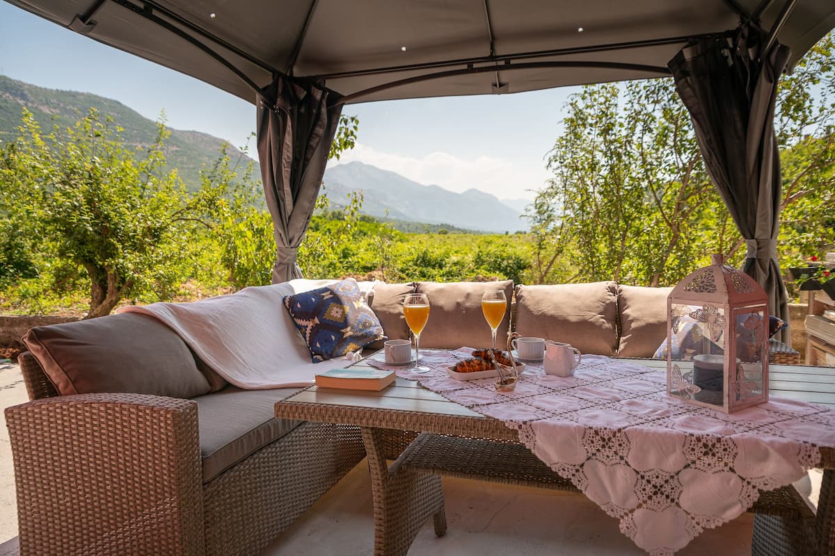 An outdoor seating area with a wicker sofa, a table with a lace tablecloth, and a lantern.