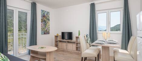 A modern living room with a sofa, a dining table with chairs, a TV, and a balcony with curtains.
