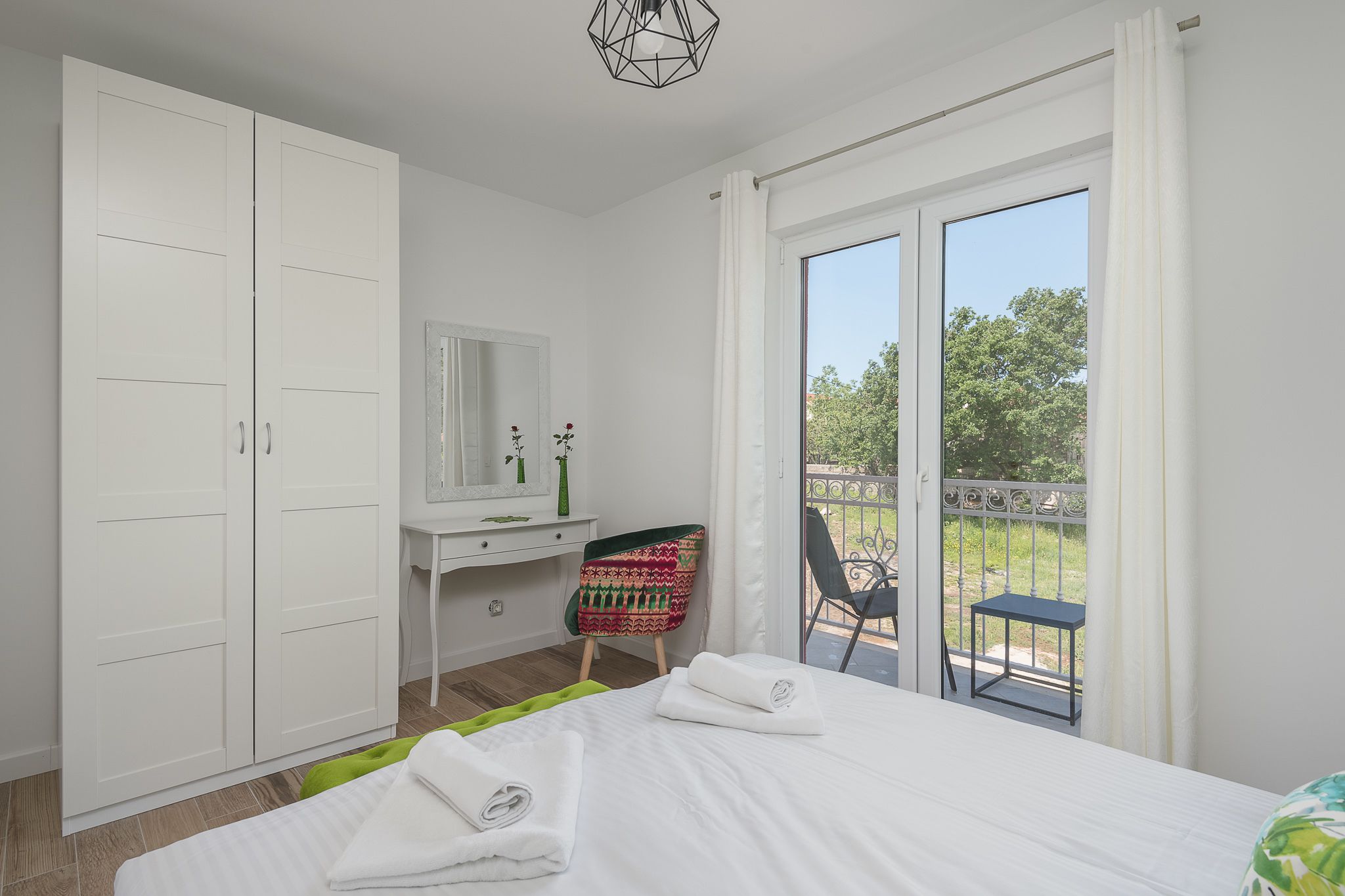 A bedroom with a bed, a desk, a chair, and a balcony with a table and chair.